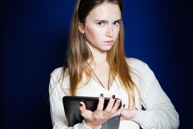 Girl with a surprised expression holds a tablet on a blue background