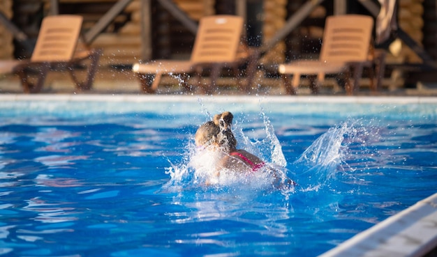 Una ragazza con gli occhialini da nuoto salta in una piscina con acqua limpida sullo sfondo di un caldo tramonto estivo