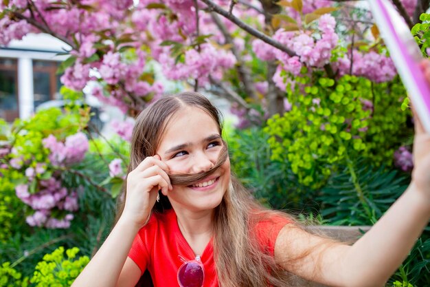 Girl with tablet laughs by blooming tree