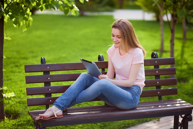 Девушка с планшетом, сидя на скамейке в парке