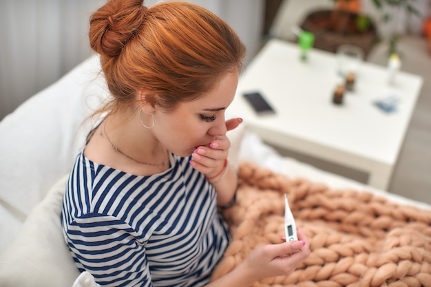 Girl with a thermometer in her hand, excitedly, checks her body temperature.