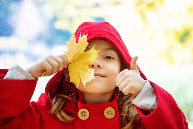 Девушка с поднятыми пальцами, держащая лист осенью.