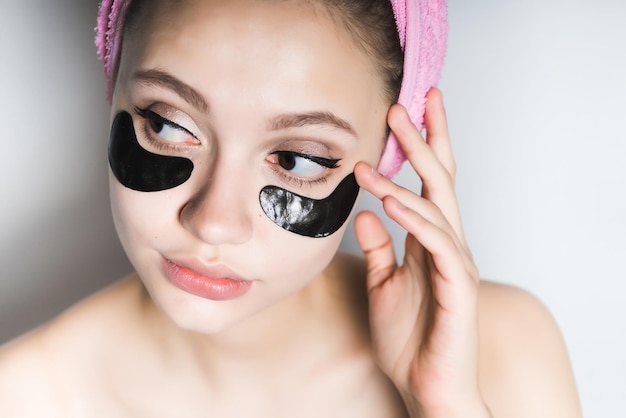 Girl with a towel on her head puts on her face a black mask