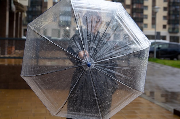 A girl with a transparent umbrella stands in the rain on a city street Climate weather