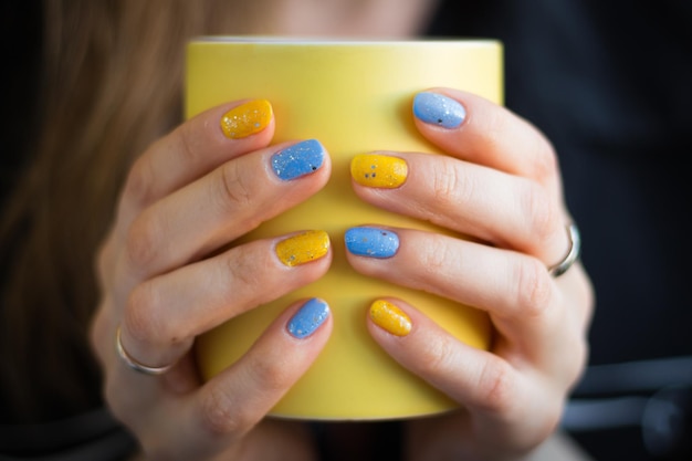 Girl with ukrainain manicure holding yellow cup Yellow mug in woman hands Morning cup of coffee