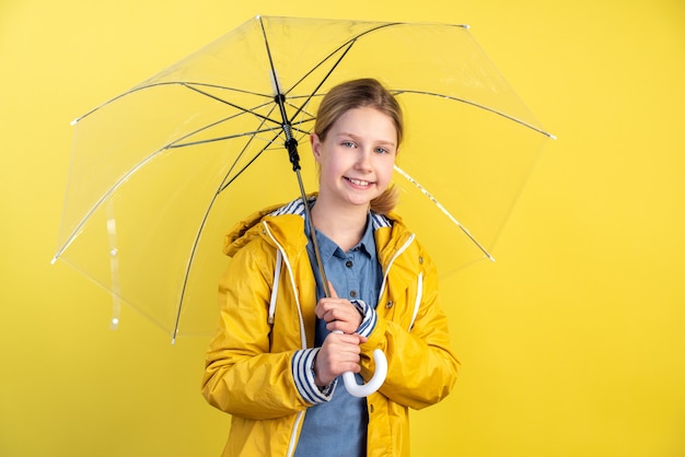 Girl with umbrella and yellow rain coat on yellow wall