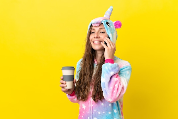 Girl with unicorn pajamas over isolated background holding coffee to take away and a mobile