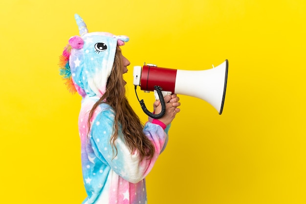 Photo girl with unicorn pajamas over isolated background shouting through a megaphone