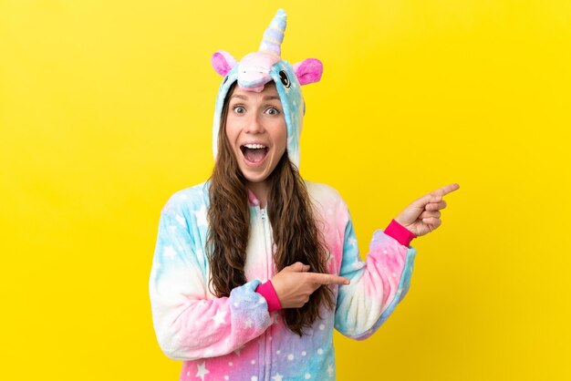 Girl with unicorn pajamas over isolated background surprised and pointing side