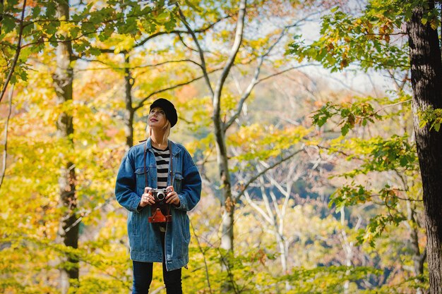 ビンテージカメラを持つ少女は、秋のシーズンに公園で休憩します。