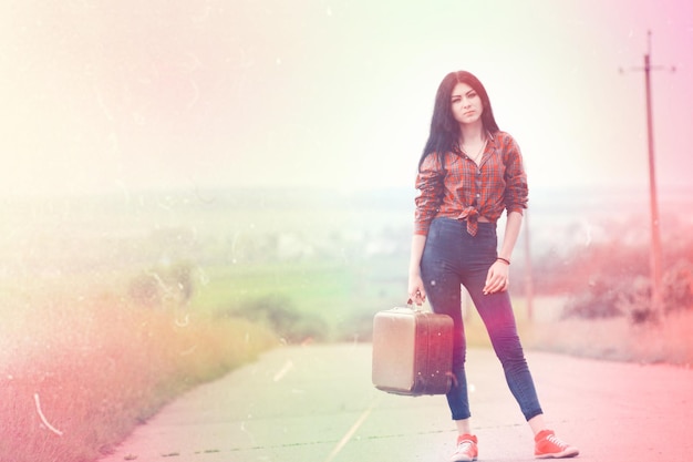 Girl with vintage suitcase is asphalt. Girl traveling hitchhiking.