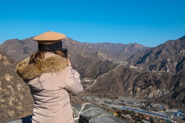 girl with warm suit hold smart mobile phone take picture of great wall china in winter on sunny day.