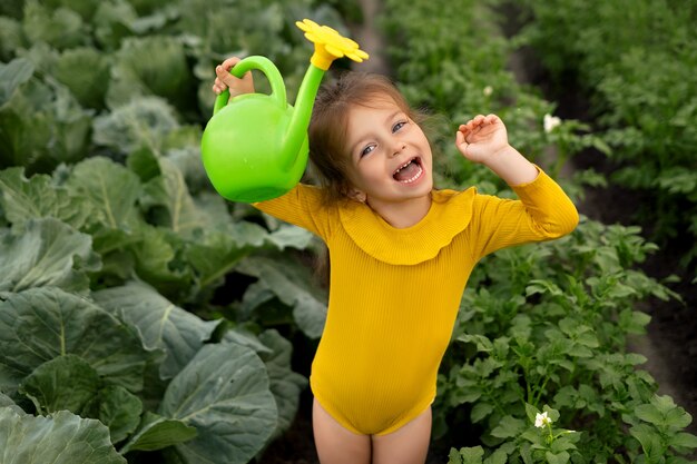 손에 물뿌리개를 들고 있는 소녀가 양배추로 채소밭에 물을 주고 있다