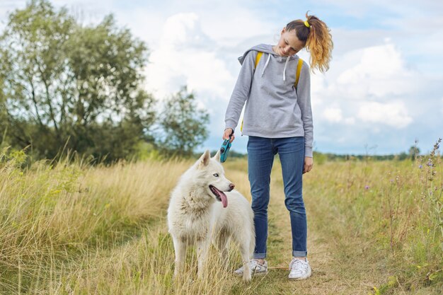 白い犬、ハスキーなペットと歩いているティーンエイジャーを持つ少女