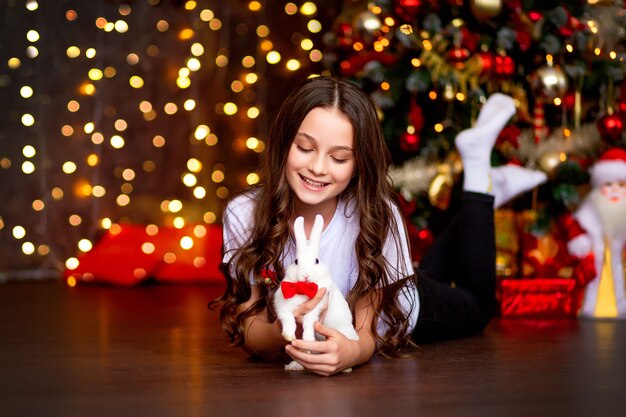 Girl with a white rabbit on the background of lights garlands from the Christmas tree