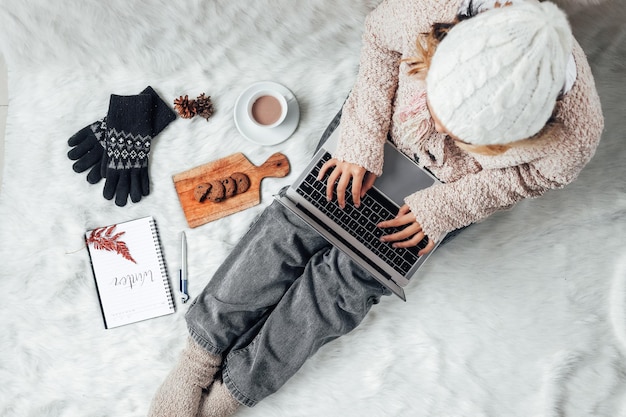 Девушка в зимней одежде работает с ноутбуком дома и наслаждается зимним сезоном