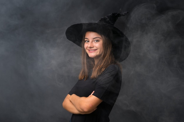 Girl with witch costume for halloween parties over isolated dark wall laughing