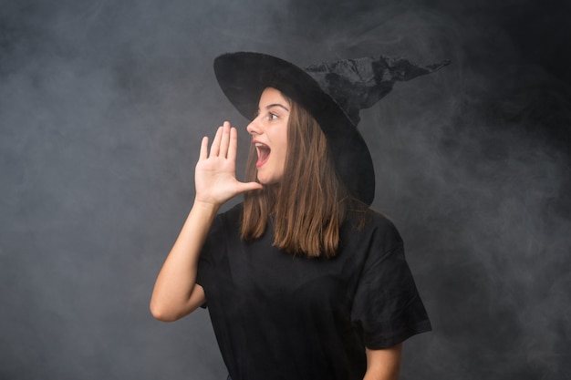 口を大きく開けて叫んで孤立した暗い壁にハロウィーンパーティーの魔女の衣装を持つ少女