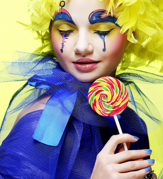 Девушка с креативным макияжем держит леденец на палочке