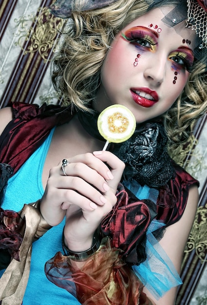 Girl with with creative makeup holds lollipop