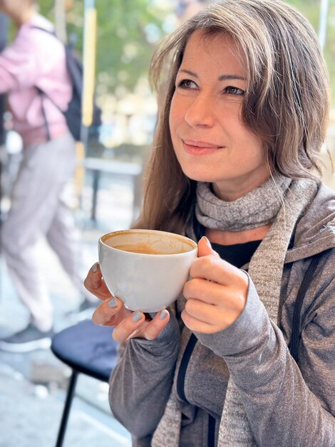 A girl woman in autumn clothes with a scarf around her neck smiles happily drinks morning coffee