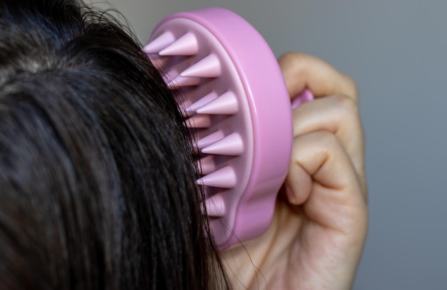 girl or woman is using pink silicone brush for scalp massage