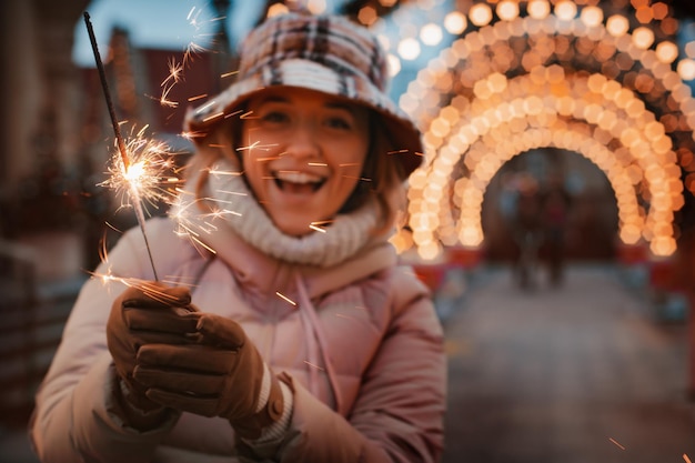 Girl woman walking with bengal sparkler Christmas market decorated with holiday lights evening.