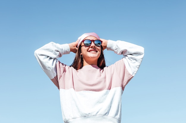 Girl woman with sunglasses, tying her pinkheadscarf.  International Breast Cancer Day, with the sky in the background. 