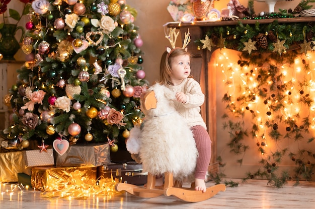 A girl on a wooden lamb gurney next to a festive Christmas tree