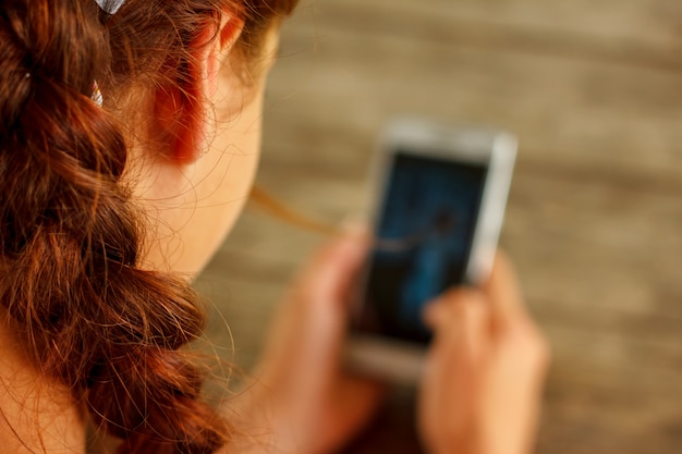 Girl at a wooden table holding a phone in her hand