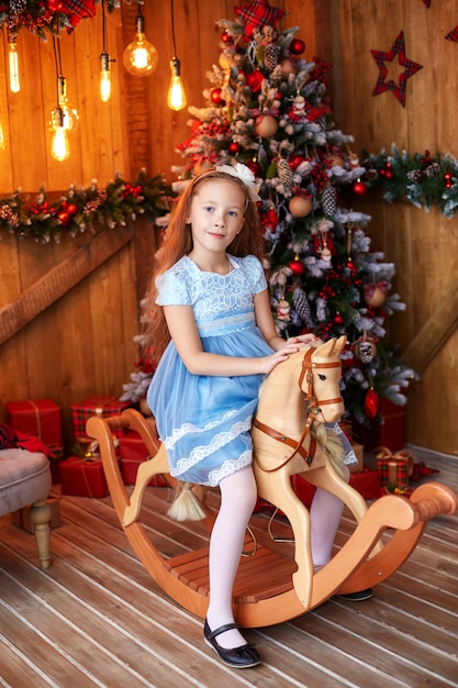 Girl on wooden toy horse near christmas tree