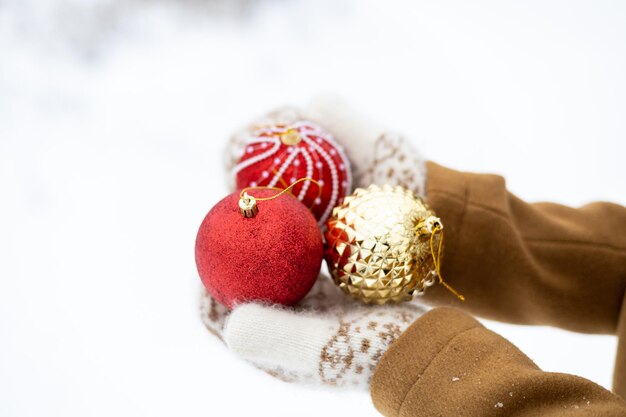 A girl in woolen mittens holds in her hands three festive\
christmas balls for the new year tree