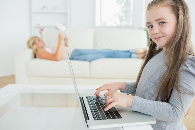 Girl working on laptop and her mother reading the newspaper