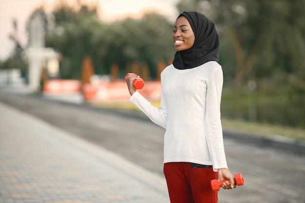 Girl working out outdoors on a stadium. Muslim woman wearing white shirt and red trousers