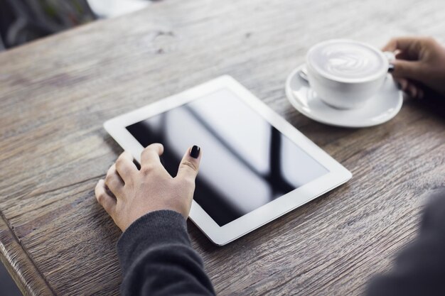 Девушка работает с цифровым планшетом и чашкой кофе на деревянном столе