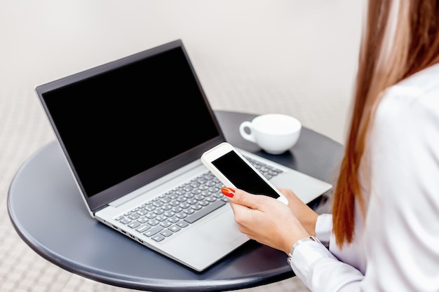 Girl working with laptop and mobile phone sitting at a table in a cafe