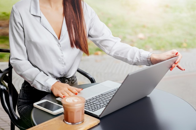 Girl working with laptop and mobile phone sitting at a table in a cafe