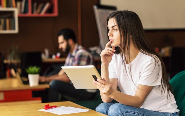 Girl working with tablet computer sitting in coworking cafe office thinking moment