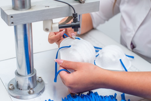 The girl works in a factory for the production of medical masks with nanofibre and solder loops with ultrasound on a machine.