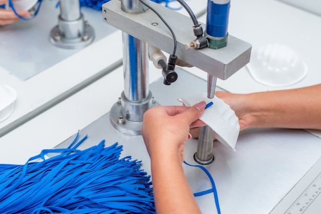 The girl works in a factory for the production of medical masks with nanofibre and solder loops with ultrasound on a machine.