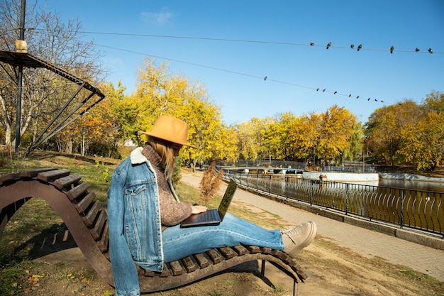 A girl works at a laptop in an autumn park