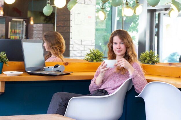 ラップトップで働く女の子。リモート作業、オンライン。のコーヒーとカフェの女の子。