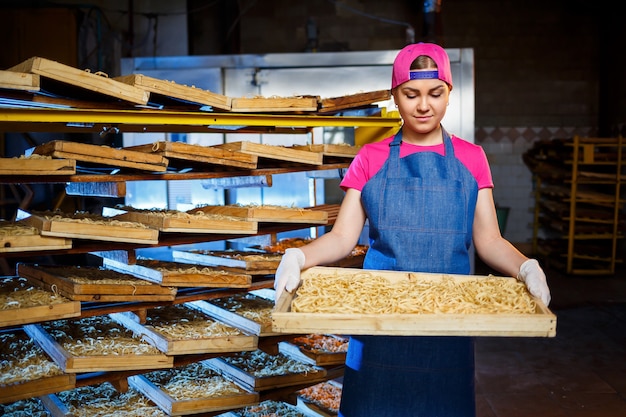 The girl works on the production of spaghetti. Making noodles. Pasta factory. Stage production of pasta. Raw noodles. Worker with a box of pasta.