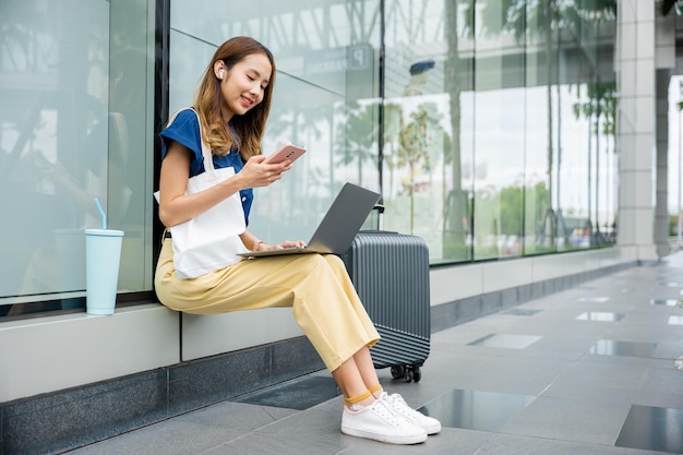 a girl works remotely from a train station with her laptop and luggage beside her