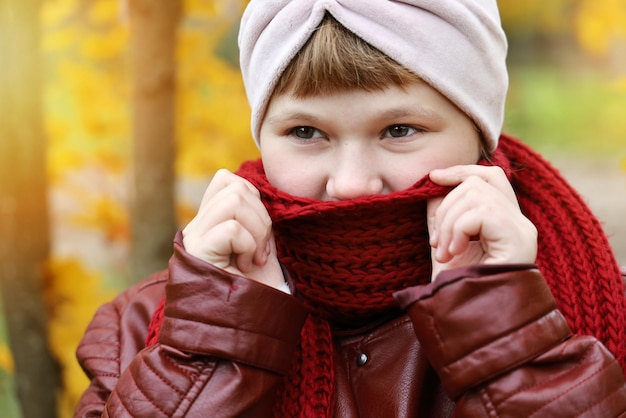 秋の屋外クローズアップ笑顔で暖かくなるように赤いスカーフに包まれた女の子