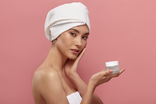 Photo girl wrapped in white hair turban holds cream jar