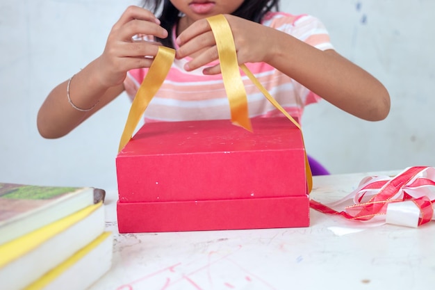 A girl wrapping a red gift with a yellow ribbon.