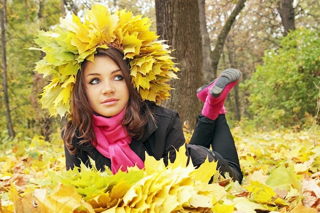 La ragazza alla corona giace su foglie gialle