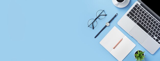 Girl write on open white book or accounting on a minimal clean light blue desk with laptop and accessories