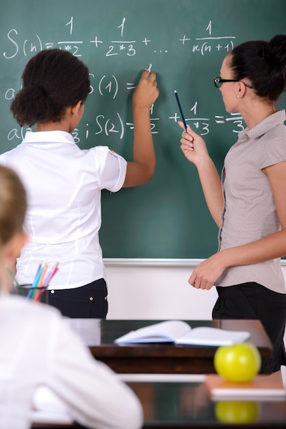 Foto la ragazza scrive alla lavagna un esempio di insegnante che aiuta.